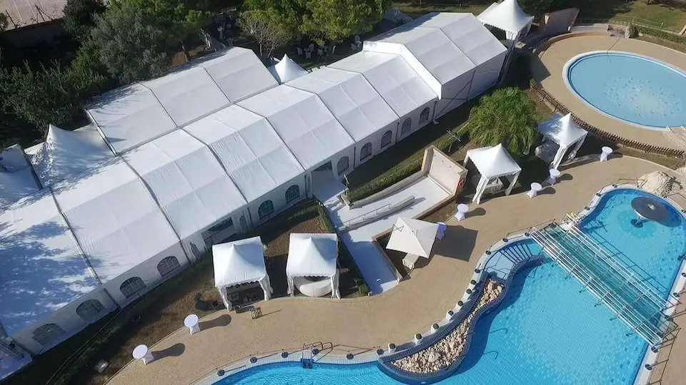 Perspectiva aérea de una carpa blanca grande y una piscina, con áreas verdes alrededor.