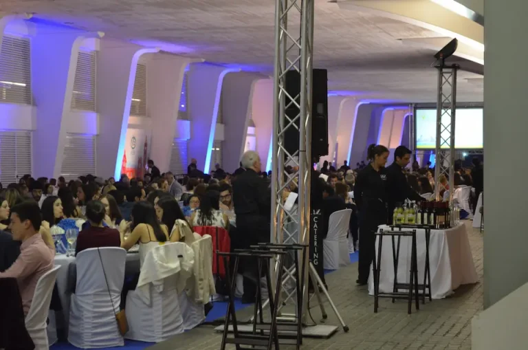 Gran sala con numerosas personas sentadas en mesas, participando en un congreso.