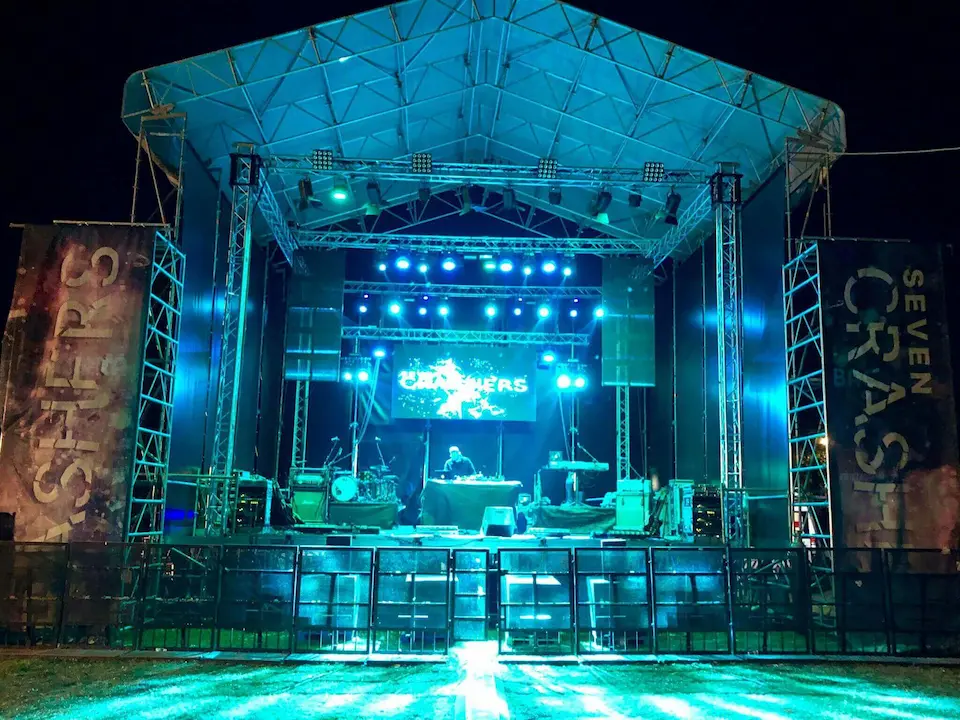Escenario iluminado para un concierto nocturno, con altavoces y luces coloridas en un ambiente festivo.