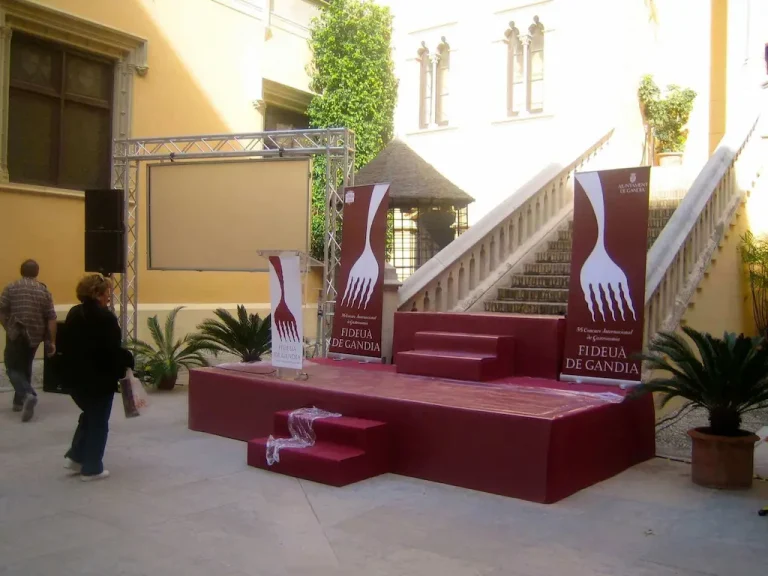 Escenario de color rojo con un tenedor blanco en el medio, simbolizando el evento culinario Fideua de Gandia