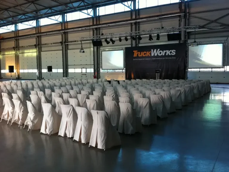 Gran sala con sillas cubiertas con manteles blancos, preparada para un evento corporativo.