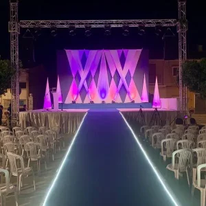 Escenario montado con sillas y un fondo púrpura y blanco para el evento Festers en Piles.