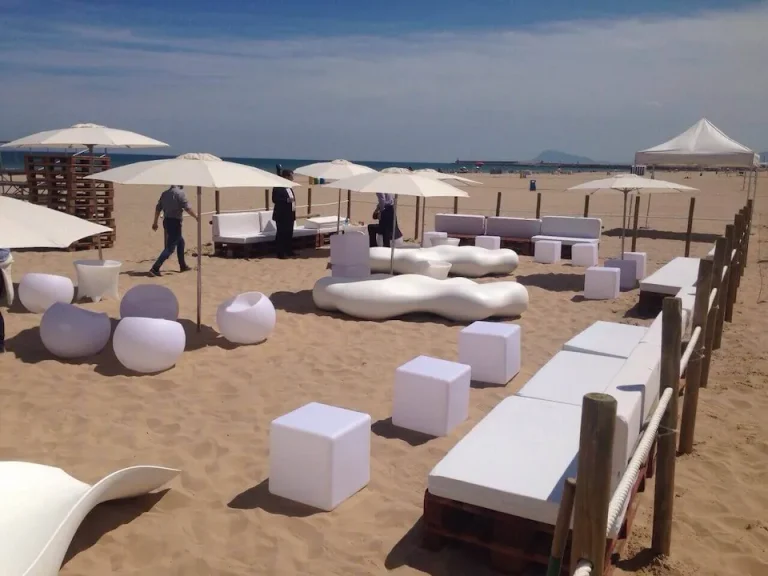 Playa de arena con sombrillas blancas y muebles blancos, creando un ambiente relajante y acogedor.