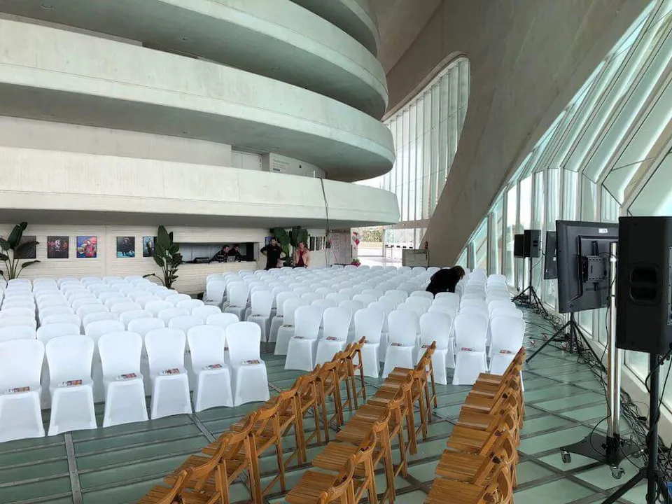 Gran sala con sillas dispuestas en filas y un escenario al fondo, lista para un evento o presentación.