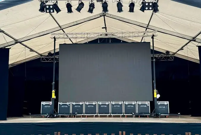 Pantalla LED grande en un escenario iluminado, rodeada de luces brillantes y un ambiente festivo.