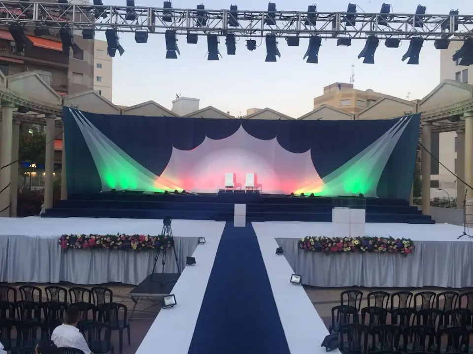 Escenario de boda con decoración elegante, incluyendo flores y sillas blancas organizadas para los invitados.