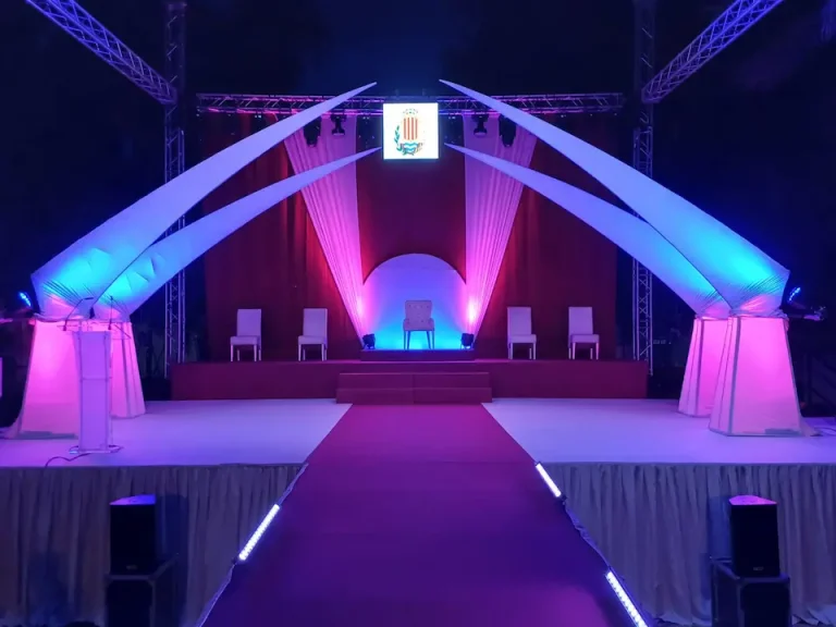 Escenario iluminado con luces moradas y rosas, preparado para una presentación.