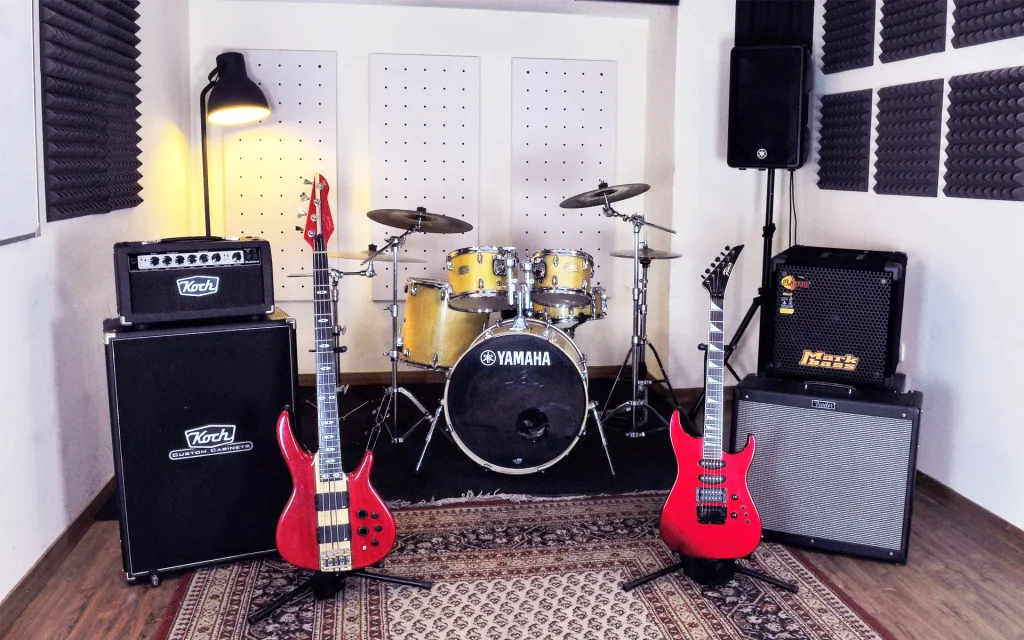 Sala de ensayo con guitarras eléctricas rojas, batería y paredes tratadas acústicamente.