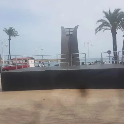 Escenario montado en la playa, cubierto con una lona negra, listo para un evento al aire libre.