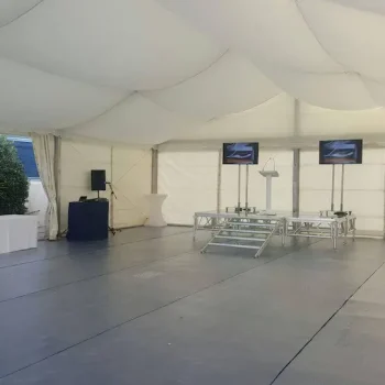 Gran carpa blanca con un escenario y altavoces visibles en su interior, preparada para un evento al aire libre.