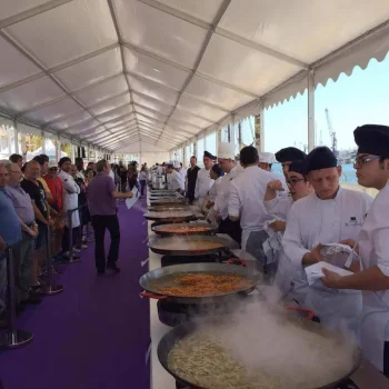Personas en uniformes blancos distribuyendo paella a los asistentes en un entorno de evento gastronómico.