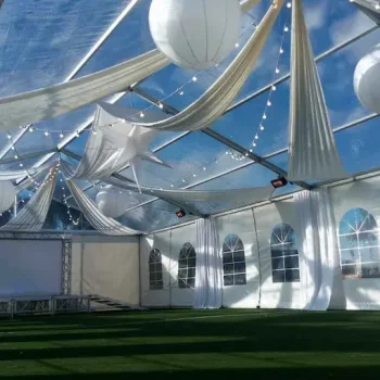 Carpa grande con cortinas blancas, adyacente a un campo de fútbol.