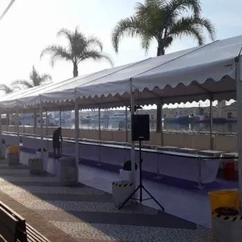 Fila de mesas y sillas dispuestas bajo una carpa blanca, lista para un evento al aire libre.