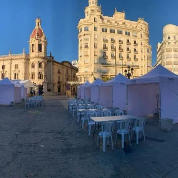 Vista de una carpa amplia con mesas y sillas blancas, situada ante un edificio.