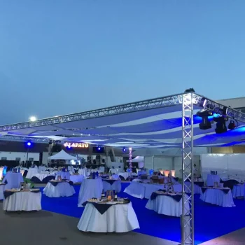 Gran evento al aire libre con mesas y sillas dispuestas para los asistentes bajo una sombra de truss.