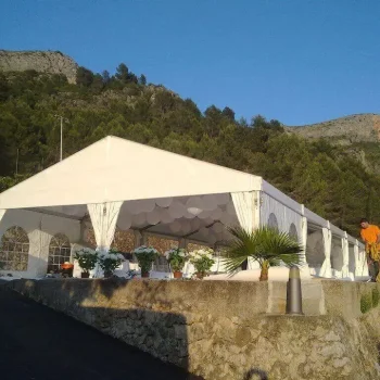 Carpa a dos aguas blanca situada en una ladera, rodeada de vegetación.