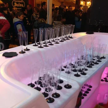 Barra de resina iluminada con luz LED, rodeada de numerosos vasos y copas en un ambiente elegante.