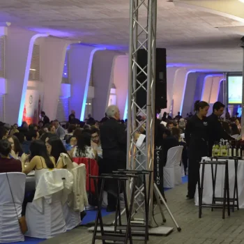 Gran sala con numerosas personas sentadas en mesas, participando en un congreso.