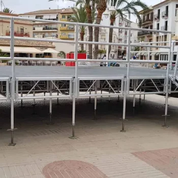Escenario de aluminio con escaleras metálicas y un automóvil estacionado frente a él.