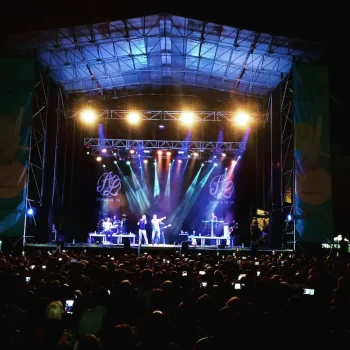 Multitud de personas disfrutando de un concierto al aire libre durante la noche, con luces brillantes en el escenario.