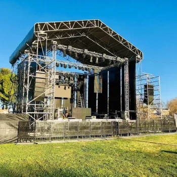 Escenario preparado para un concierto al aire libre, con césped y luces brillantes en el fondo.