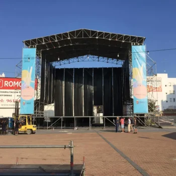 Escenario amplio con varias personas de pie alrededor, preparándose para una presentación o evento.