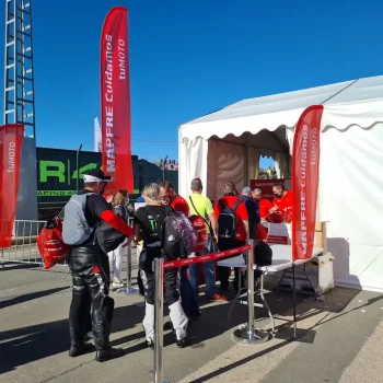 Grupo de personas de pie frente a una carpa en un evento deportivo al aire libre.