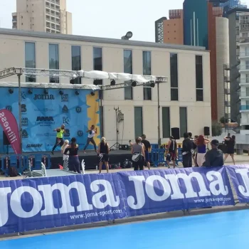 Escenario con un grupo de personas, en un evento deportivo, ante un edificio.