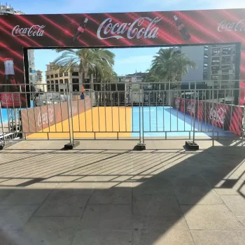 Valla con un anuncio de Coca-Cola situada ante un edificio en un evento deportivo.