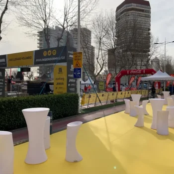 Área de evento deportivo con alfombra amarilla y mesas y sillas blancas organizadas.