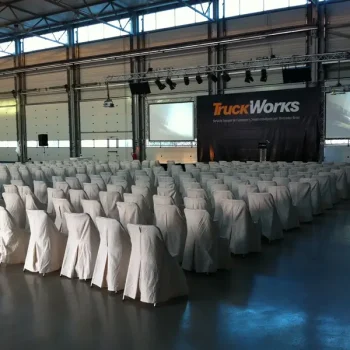 Gran sala con sillas cubiertas con manteles blancos, preparada para un evento corporativo.