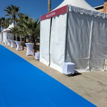 Alfombra azul junto a carpas blancas, ubicadas en el entorno de una feria.