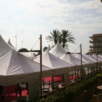 Fila de carpas blancas dispuestas en una feria al aire libre, con un cielo despejado de fondo.