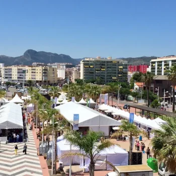 Vista de la playa con carpas en una feria, rodeada de gente disfrutando del ambiente festivo.