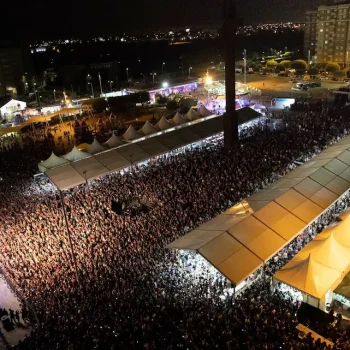 Gran cantidad de asistentes en un concierto, con luces brillantes y un escenario visible al fondo.