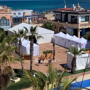 Vista de una playa con carpas y palmeras, mostrando un ambiente festivo y veraniego.