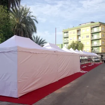 Fila de carpas blancas dispuestas en una feria al aire libre, con un cielo despejado de fondo.