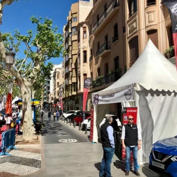 Vista de una calle donde se observa una carpa de feria y automóviles aparcados.