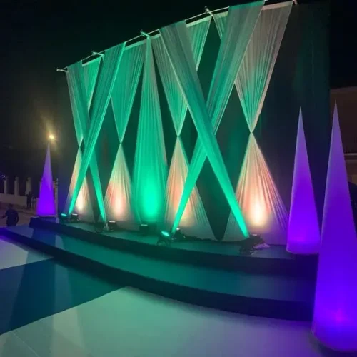 Escenario iluminado con luces verdes y moradas, decorado con un telón de fondo para el evento Festers en Piles.