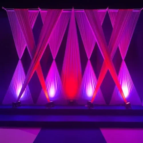 Escenario iluminado con luces moradas y rosas, decorado con cortinas, durante el evento Festers en Piles.