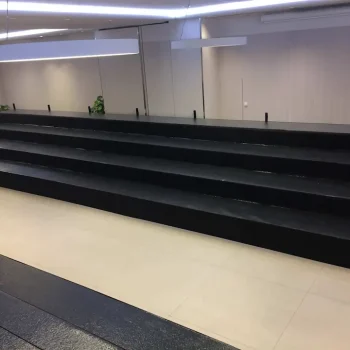 Gradas de color negro en un espacio grande, con una pared blanca que las acompaña.