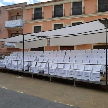 Gradas con sillas dispuestas bajo un toldo, ubicadas frente a un edificio.