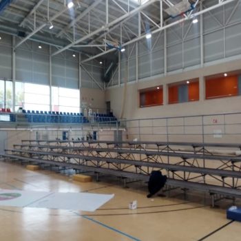 Vista de un gimnasio amplio con gradas y un gran banner en la pared frontal.