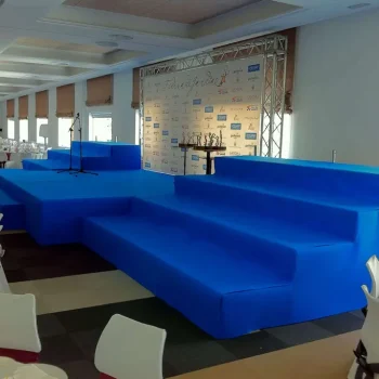 Escenario grande de color azul, preparado para un evento, con gradas visibles en primer plano.