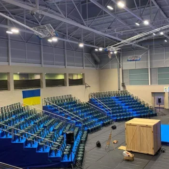 Vista de gradas en un gimnasio, con asientos y piso en tonos azules.