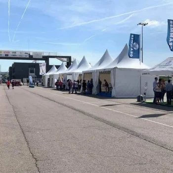 Una fila de tiendas de campaña con personas de pie frente a ellas, en un entorno al aire libre.