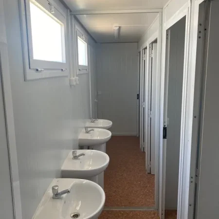 Fila de lavabos en un baño, con un inodoro visible al fondo.