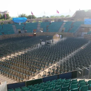 Arena vacía con sillas verdes y un escenario al fondo, lista para un evento o espectáculo.