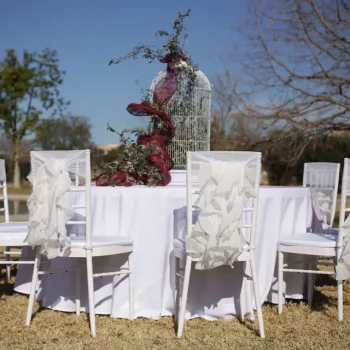 Mesa con sillas blancas y un jarrón de flores coloridas en el centro.