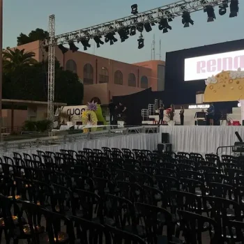 Escenario al aire libre con sillas dispuestas y una pantalla grande al fondo, listo para un evento.